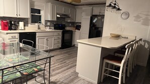 A modern kitchen with white cabinets, a dining area with a glass table, and a ceiling fan. - Beautiful Beach House In Fort Morgan !  (Gulf Shores)