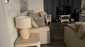 A living room with a sofa, a chair, a small table with a lamp, and a television in the background. - Beautiful Beach House In Fort Morgan !  (Gulf Shores)