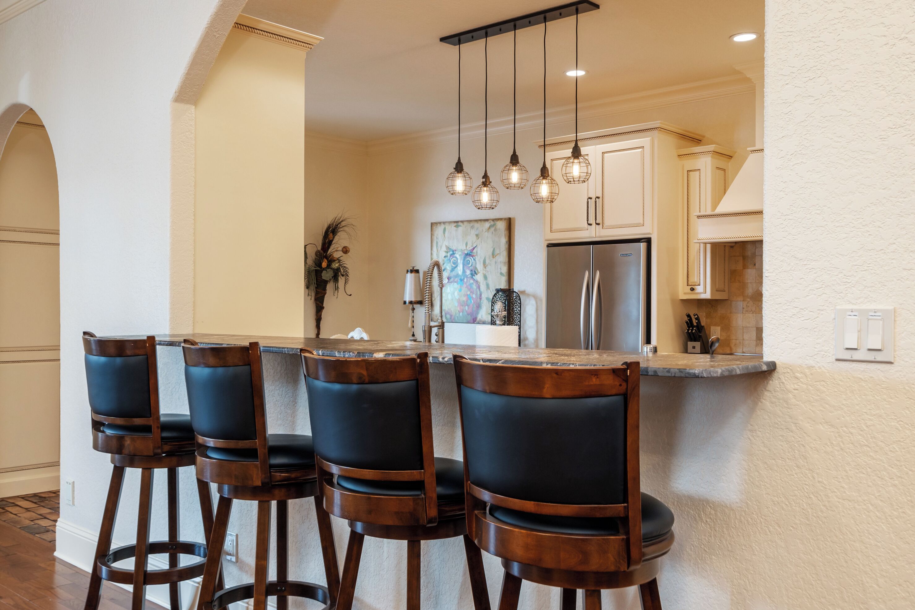 Une cuisine dotée d’un îlot central, de tabourets de bar, de luminaires suspendus et d’un réfrigérateur.