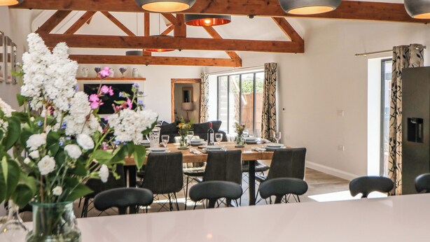 A dining area with a large table, multiple chairs, and hanging pendant lights. - Langley Barn (Ashbourne)
