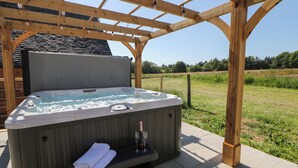 A hot tub under a wooden pergola with a grassy field in the background. - Langley Barn (Ashbourne)