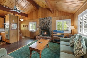 A cabin interior with a stone fireplace, wooden walls, a dining area, and a television. - Snowridge (Big Bear City)