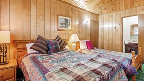 A wooden-paneled room with a large bed, two bedside tables, a nightstand, and a mirror. - Snowridge (Big Bear City)