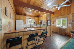 A cabin-style kitchen with wooden walls, a bar area with chairs, and a ceiling fan. - Snowridge (Big Bear City)