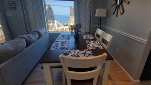 Uma área de refeições com uma mesa posta para dois, um sofá e vista para o mar.