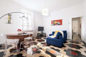 A modern living room with a blue sofa, a dining area with a round table and chairs, and a patterned floor.