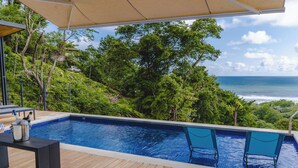 A swimming pool with a wooden deck, two chairs, and a table with a bottle and glass. - LeSuite Santa Teresa  (Cóbano)