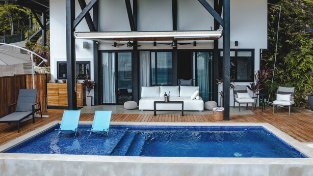 A modern outdoor pool area with a wooden deck, two lounge chairs, a sofa, and a dining table. - LeSuite Santa Teresa  (Cóbano)
