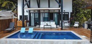 A modern outdoor pool area with a wooden deck, two lounge chairs, a sofa, and a dining table. - LeSuite Santa Teresa  (Cóbano)