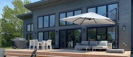 A modern two-story house with a large deck, outdoor seating, and a grill.