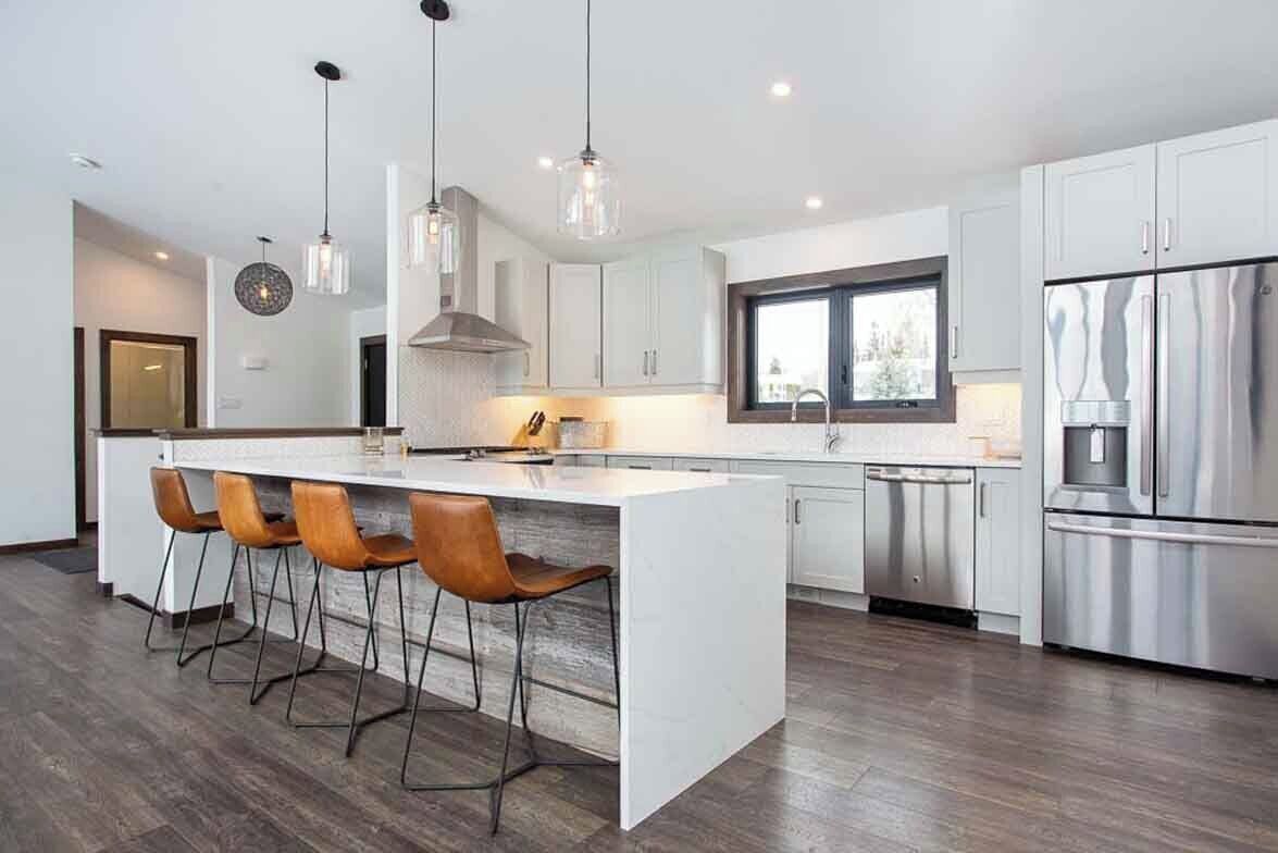 A modern kitchen with a central island, bar stools, stainless steel appliances, and pendant lighting.