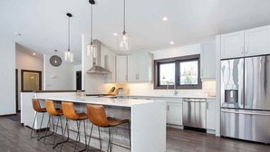 A modern kitchen with a central island, bar stools, stainless steel appliances, and pendant lighting.