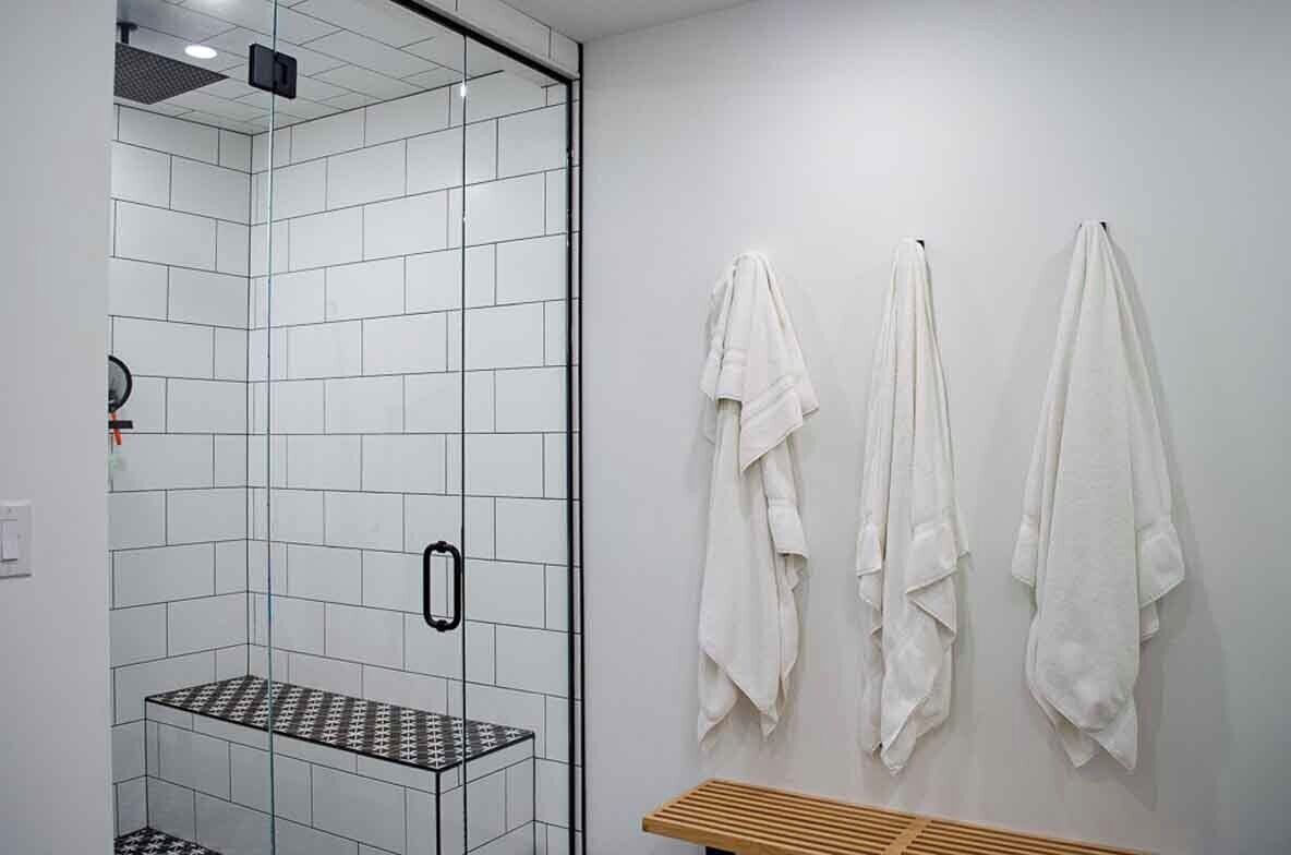 Une salle de bain moderne avec une douche à parois de verre, un banc et trois serviettes accrochées au mur.