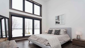 A bedroom with a large bed, a nightstand, a mirror, and a view of a snowy landscape through large windows.