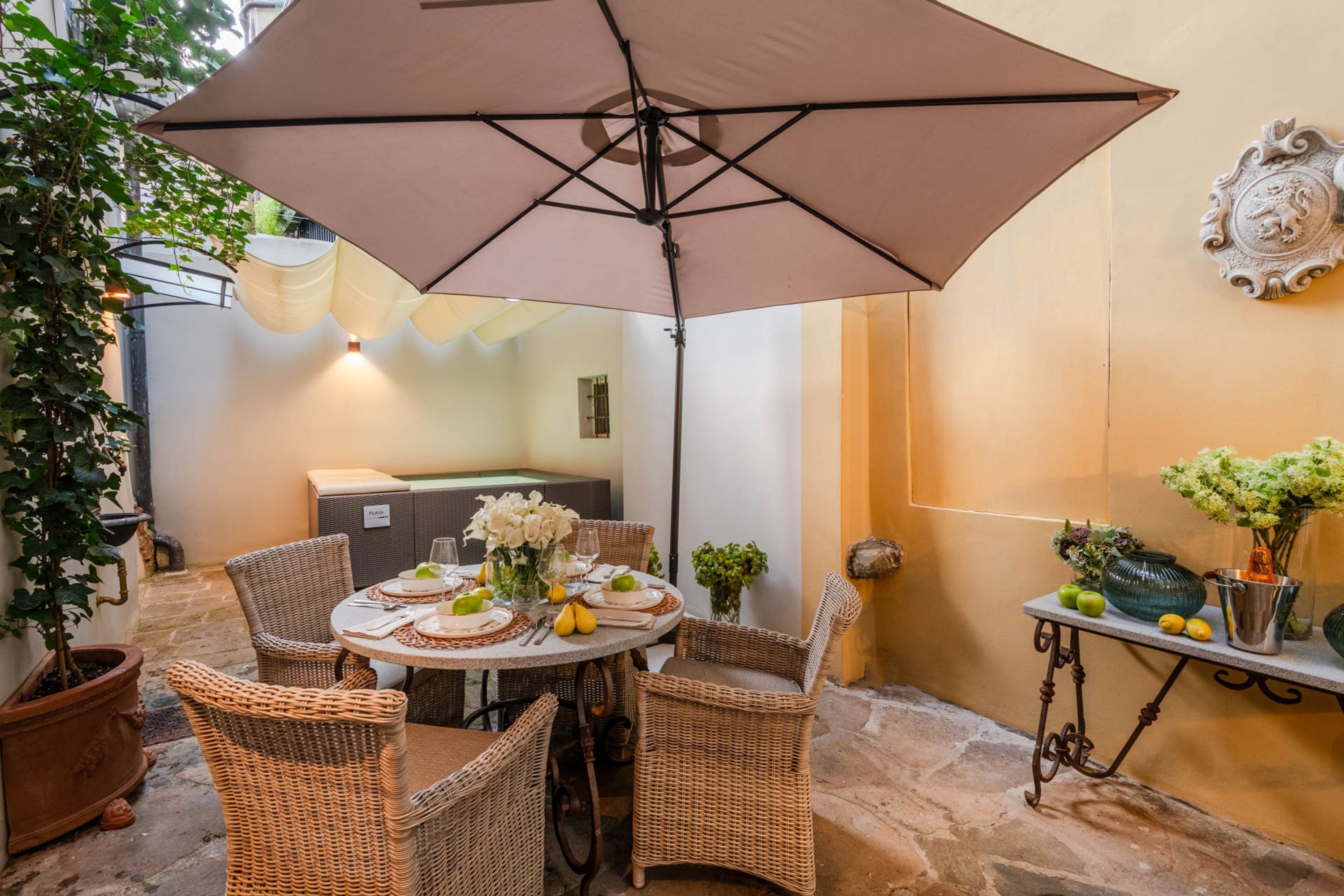 A round table with wicker chairs, a large umbrella, and a vase with flowers.