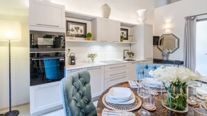 A modern kitchen with white cabinetry, a blue oven, and a dining area with a round table set for six. - Gallo Cedrone a Home With Outdoor (Lucca)