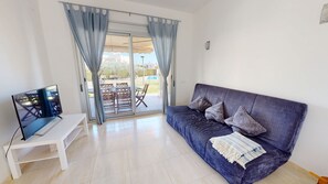 A living room with a sofa, TV, and a sliding glass door leading to an outdoor area.