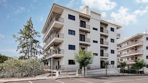 Un edificio residencial de varios pisos con balcones, un estacionamiento y áreas verdes circundantes.