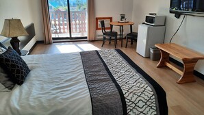 A hotel room with a bed, a desk, a chair, a TV, and a balcony with a view. - Alpen Motel (Radium Hot Springs)