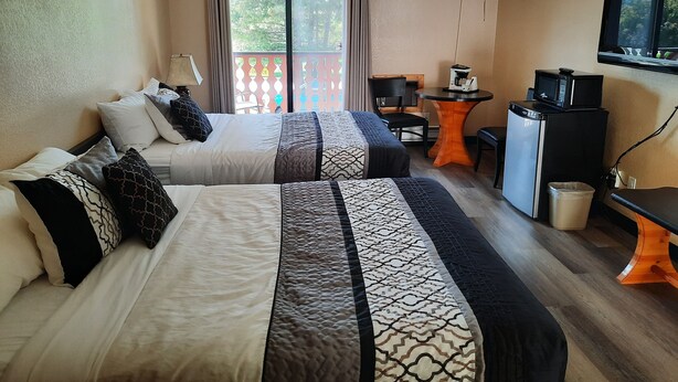 A hotel room with two beds, a small table with a coffee maker, a TV, and a trash bin. - Alpen Motel (Radium Hot Springs)