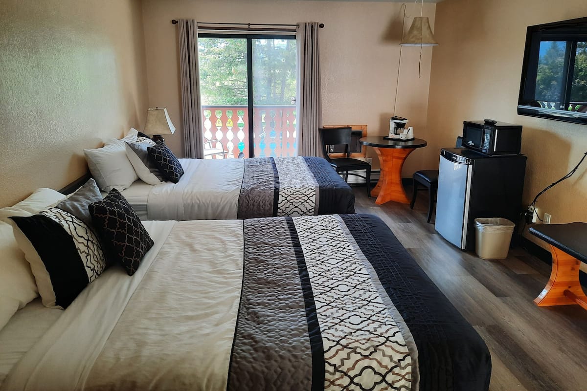 A hotel room with two beds, a small table with a coffee maker, a TV, and a trash bin.