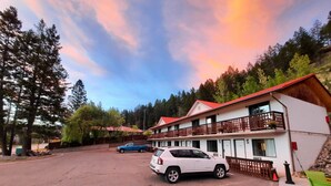 A motel with a red roof and white walls, a parking lot, and a scenic view of trees and mountains. - Alpen Motel (Radium Hot Springs)