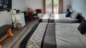 A hotel room with two beds, a desk with a chair, a TV, a microwave, and a window with curtains. - Alpen Motel (Radium Hot Springs)