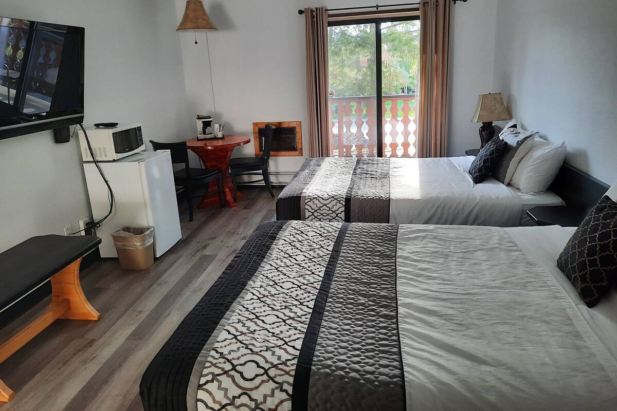 A hotel room with two beds, a desk with a chair, a TV, a microwave, and a window with curtains.