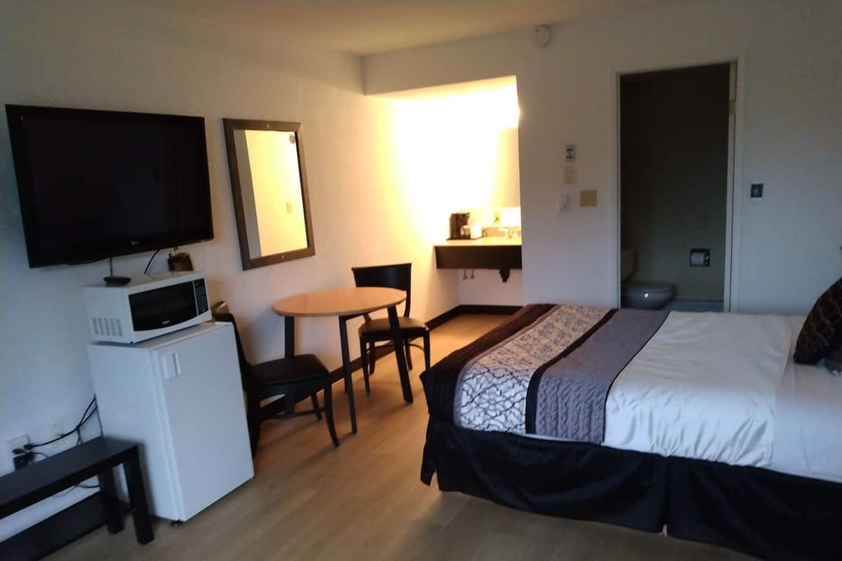 A hotel room with a bed, a desk with a chair, a microwave, a television, and a bedside table.