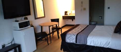 A hotel room with a bed, a desk with a chair, a microwave, a television, and a bedside table.