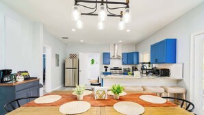 A modern kitchen with blue cabinets, a dining area with a wooden table and chairs, and a central island with a sink.