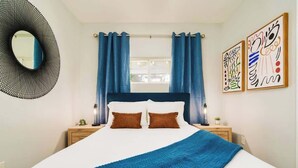 A bedroom with a bed, curtains, a round mirror, and two wall art pieces.