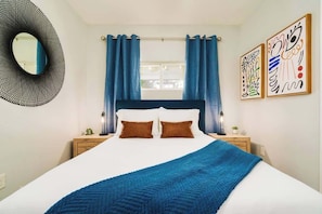 Ein Schlafzimmer mit einem Bett, Vorhängen, einem runden Spiegel und zwei Wandbildern.