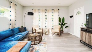A living room with a blue sofa, two armchairs, a coffee table, a TV, and a large plant.