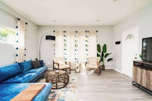 Ein Wohnzimmer mit einem blauen Sofa, zwei Sesseln, einem Couchtisch, einem Fernseher und einer großen Pflanze.