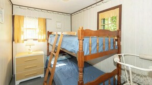 Una habitación con literas, una mesita de noche con lámpara y una ventana con cortinas.