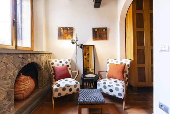 A cozy living room with a stone fireplace, two polka-dotted chairs, a small ottoman, and a wooden cabinet.