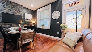 A modern living room with a leather sofa, a dining area with a wooden table and chairs, a large clock on the wall, and a window with a view. - Spacious & Cozy with luxury furnitures /1 King+2 Queen/-University City (Philadelphia)