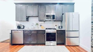 A modern kitchen with grey cabinets, a stainless steel refrigerator, a microwave, an oven, and a dishwasher. - Spacious & Cozy with luxury furnitures /1 King+2 Queen/-University City (Philadelphia)