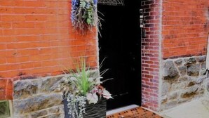 A brick building with a black door and a 'WELCOME' sign above it. There is a planter with flowers in front of the door. - Spacious & Cozy with luxury furnitures /1 King+2 Queen/-University City (Philadelphia)