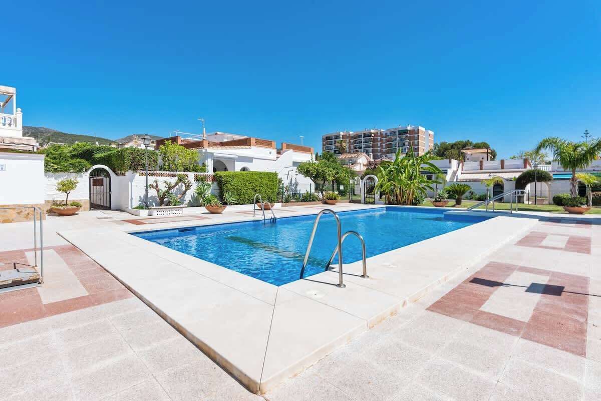 A swimming pool with a clear blue water, surrounded by a tiled deck and potted plants.