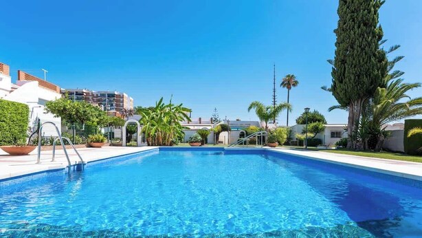A rectangular swimming pool with clear blue water, surrounded by potted plants and palm trees. - Family Apartment with Pool by Costarentals - Ref 218 (Torremolinos)
