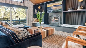 A cozy living room with a fireplace, wooden furniture, and a large window overlooking a deck.