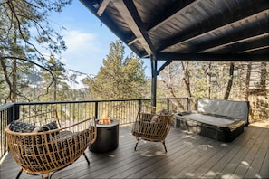 A wooden deck with a fire pit, two wicker chairs, and a hot tub. - Ski View Chalet (Big Bear Lake)
