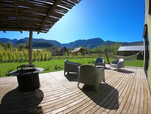 A wooden deck with a barbecue, outdoor chairs, and a hammock overlooking a mountainous landscape. - Éden Bed & Nature (Praia Grande)