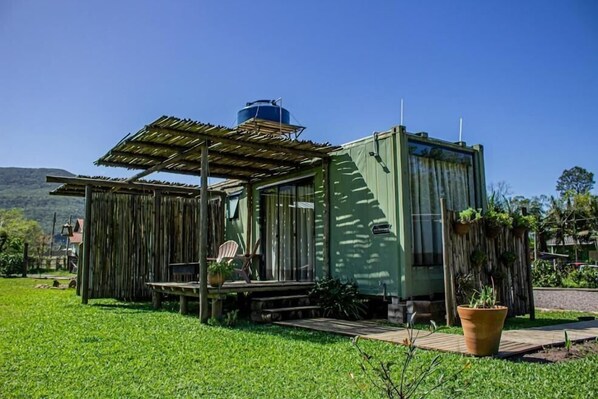A rustic cabin with a wooden deck, a large water tank on the roof, and a green exterior wall. - Éden Bed & Nature (Praia Grande)