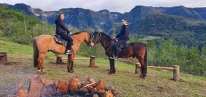 Two people on horses in a natural setting with mountains in the background. - Éden Bed & Nature (Praia Grande)