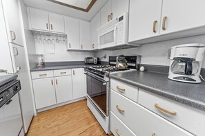 Uma cozinha moderna com armários brancos, fogão a gás, micro-ondas, máquina de café e torradeira.