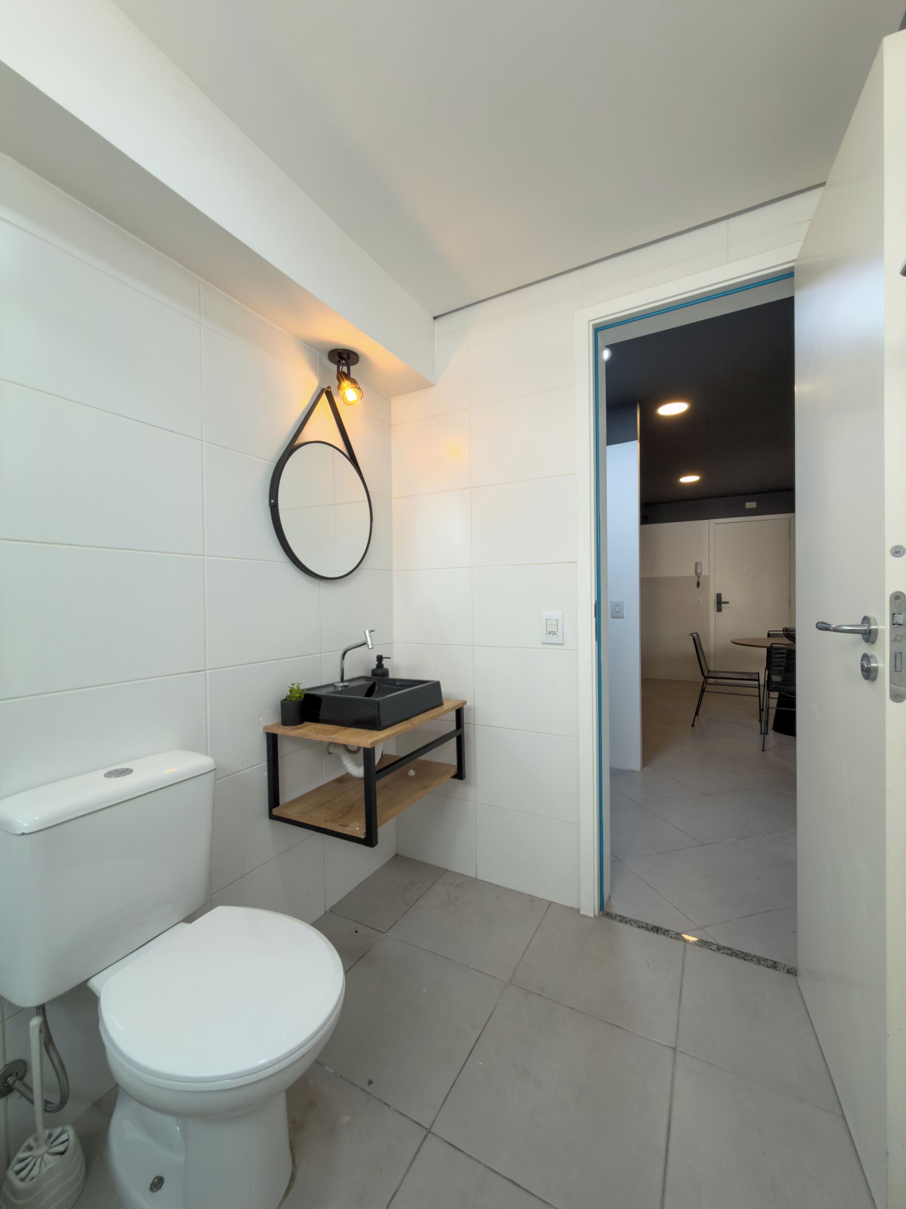 Un baño moderno con inodoro, lavamanos con estante de madera y espejo con luz.