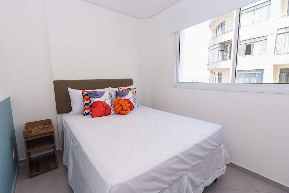 Ein Schlafzimmer mit Bett, Fenster und Blick auf ein Gebäude.